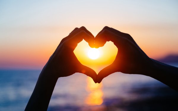 Hands forming a heart shape with a sunset backdrop, symbolizing romance and love.