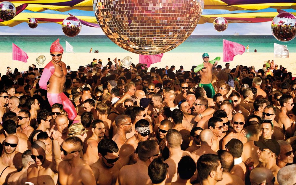 Shirtless men dancing under a disco ball at an LGBTQ party on Miami Beach