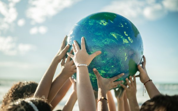 A group of children holding up a large ball-like planet earth on the beach, for Earth Day